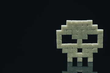 Skull with sugar cubes on a  black glass table background. Concept sweet kill or unhealthy diet .
