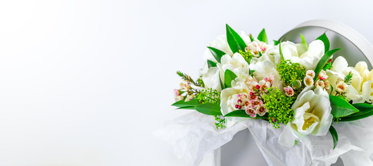 A box with white tulips and ornamental plants on a white background. Spring flowers.  Place for text. 