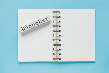 Clean spiral note book for notes and messages and december wooden calendar bar on blue background. Minimal business flat lay