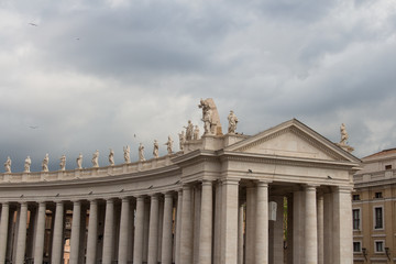 Upper facade of Peter's Square Colonnade with rainy clouds on background, Vatican city state, Italy.