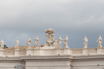 Fototapeta na wymiar Group of statues of Peter's Square Colonnade with rainy clouds on background, Vatican city state, Italy.