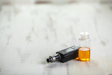 Vape objects. Electronic cigarette and jar with e-liquid on a light wooden table.
