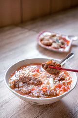 Beef noodle - Taiwan ramen meal with tomato sauce broth in bowl on bright wooden table, famous chinese style food, close up, top view, copy space