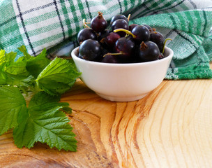 Fresh ripe currants berries. Redcurrant, blackcurrant fruit in white bowl with green leaves on wooden background. Close up, selective focus, vertical.