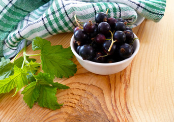 Fresh ripe currants berries. Redcurrant, blackcurrant fruit in white bowl with green leaves on wooden background. Close up, selective focus, vertical.