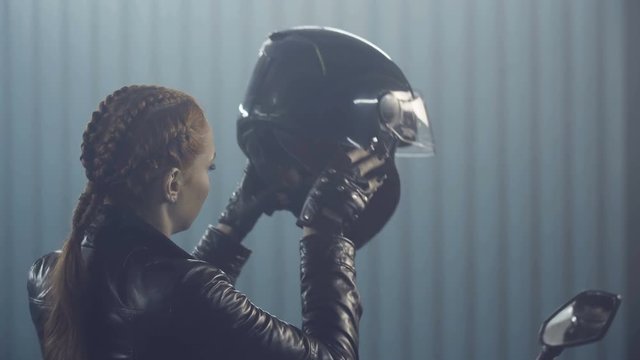 Brutal biker girl in a stylish black leather jacket and gloves sits on a motorcycle and wears helmet. Preparation in the night races. Moto service. Frame for the film.