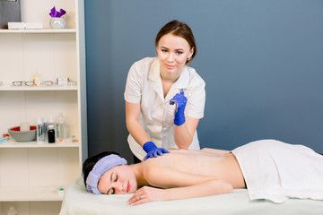 Fototapeta premium Woman take back massage in spa salon with young beautician. Young smiling medical cosmetologist looking at camera at work.