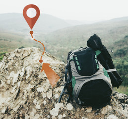 Backpack on peak of rocky mountain with scheme of track and pin.