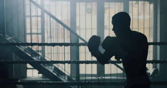 Cinematic slow motion shot of a professional young muscular shirtless african man is practicing shadow boxing work out in a gym with ring. 