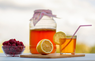 Kombucha  in a jar on a light wooden table against the sky, a glass filled with Kombucha   with raspberries.