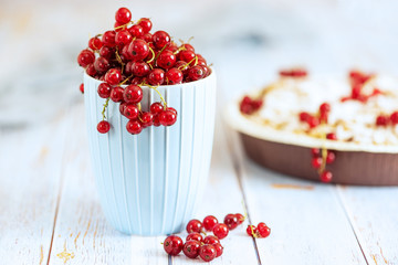 Fresh red currants in light blue cup on light wooden table