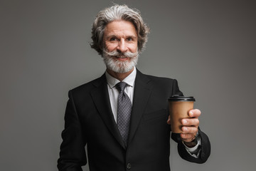 Image of happy adult businessman wearing formal black suit smiling and holding paper cup