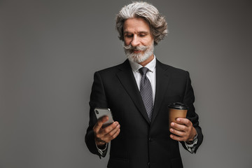 Image of smiling adult businessman wearing formal black suit holding paper cup and smartphone