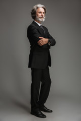 Full length image of unshaven adult businessman wearing formal black suit standing at camera with arms crossed