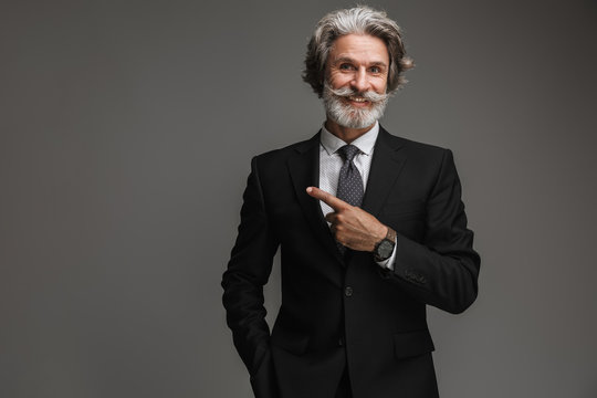 Image of handsome adult businessman wearing formal black suit smiling and pointing finger at copyspace