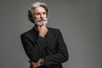Image of bearded adult businessman wearing formal black suit looking aside at copyspace