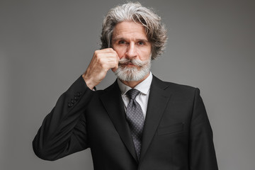 Image of handsome adult businessman wearing formal black suit looking at camera and touching his mustache