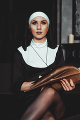 Beautiful young nun in religion black suit holds Bible and posing on camera with big book on a...