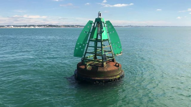 A green starboard hand lateral buoy / mark / post in shipping channel filmed from sailing yacht on calm sunny day with tide flowing.
