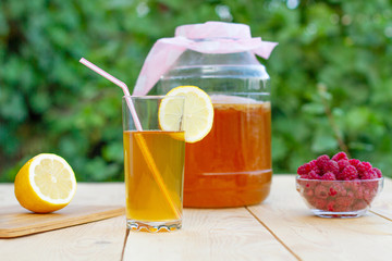 Glass jar with Kombucha, poured glass with Kombucha and raspberries in the summer garden.