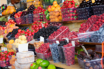 Containers with different ripe berries and fruit at market