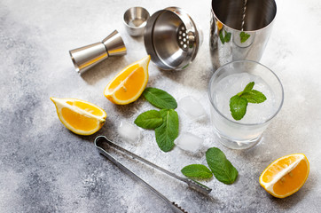 Cocktail shaker and bar tools. Ingredients for a cold alcoholic cocktail. Mojito cocktail. Lemon, mint, ice, rum. Top view, vertical, gray background, copy space