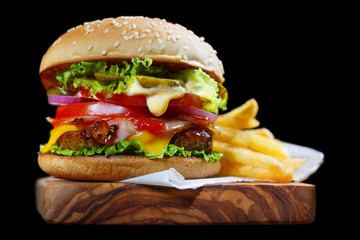 Delicious burger containing cheese, bacon, onion, cucumbers, tomatoes and lettuce, isolated on black background