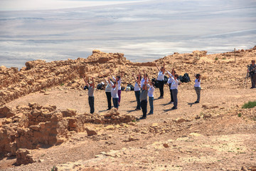 A group of people raises his arms to the sun at Masada's ruins, Israel