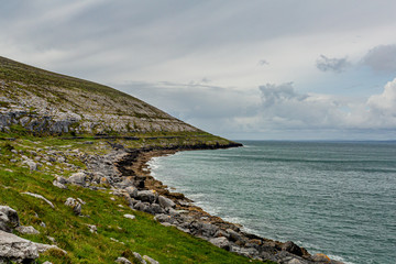 Irish landscape of the sea and a rocky limestone mountain between Bothar nA hAillite and Fanore, geosite and geopark, Wild Atlantic Way, cloudy spring day in County Clare in Ireland
