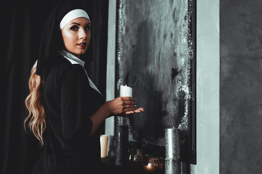Young catholic nun is holding candle in her hands. Photo on black background. Side view.