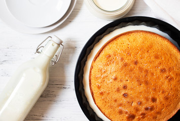 Traditional dessert Three Milk, Tres Leches or Trilece.  Dessert is served on a white wooden table with milk in a bottle and a cup, with white plates. Top view