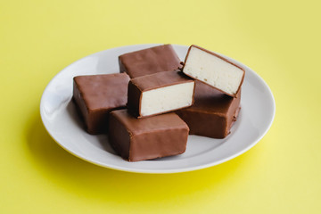 Chocolate sweets with white souffle on a plate on a yellow background.