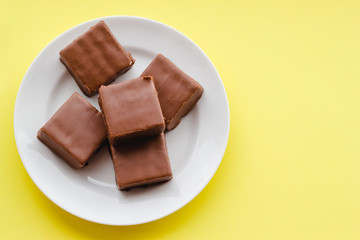 Chocolate sweets on a plate on a yellow background.