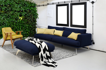Industrial interior od living room with navy scandinavian sofa and wall with greenery.  Frames with mock up. - obrazy, fototapety, plakaty
