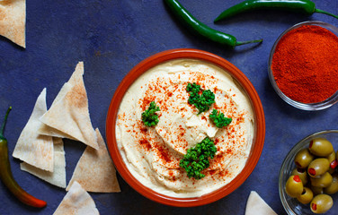 Healthy homemade hummus served with paprika powder, pita bread, olives and parsley. Middle Eastern cuisine, Israeli cuisine, Levanese cuisine, Levantine cuisine. Dark background. Top view