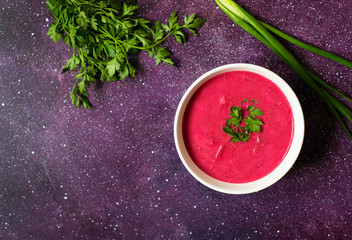 Cold Creamy Beetroot Soup, Beetroot Gazpacho Served in a White Plate with Bread and Fresh Herbs. Bright Purple Background. Vegetarian, Clean Eating Food Concept. Copy Space. Top View