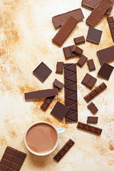Assortment of different types of chocolate and cup of cocoa on a light marble background. Top view, flat lay. Space for text
