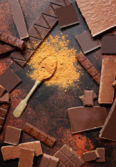 Assortment of different types of chocolate and cocoa powder on a dark background. Top view, flat lay. Space for text