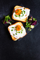 Sandwich with ham, cheese and egg. A traditional French croque-madame sandwich served with lettuce leaves on a black plate. Popular French cafe meal. Black background. Top view. Space for text