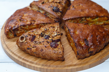  homemade banana pie with nuts, dried apricots and raisins, cut into pieces, on a wooden board