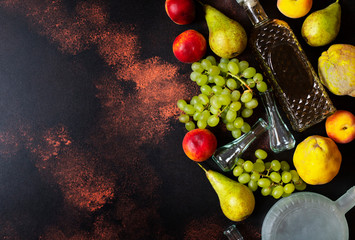 Rakia or Rakija the traditional balkan fruit brandy. The fruits of which produce Rakia. Fruits, bottles and glasses for alcohol. Top view. Dark vintage background. Space for text