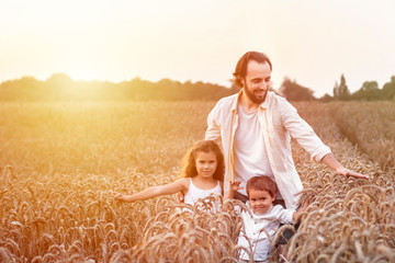 Happy family, father, son and girl in straw hat in wheat field at sunset. The concept of organic farming and healthy lifestyle, healthy food, happiness and joy