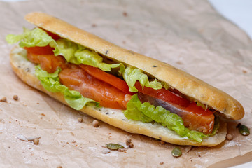 Sandwich with salmon and vegetables, lettuce and sauce in homemade bun. On kraft paper background.