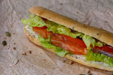 Sandwich with salmon and vegetables, lettuce and sauce in homemade bun. On kraft paper background.