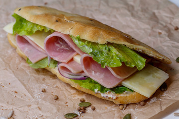 Sandwich with ham, cheese, lettuce and sauce in homemade bun. On kraft paper background.