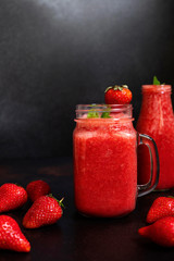 Strawberry smoothies or strawberries with ice in a jar. A refreshing summer drink. Black background. Front view. Copy space