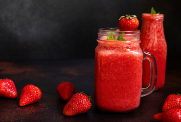 Strawberry smoothies or strawberries with ice in a jar. A refreshing summer drink. Black background. Front view. Copy space