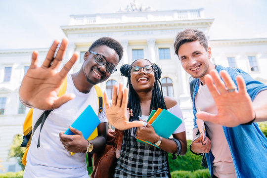 Summer holidays, education, campus and teenage concept - group of multiethnic students or teenagers waving hands over university building.