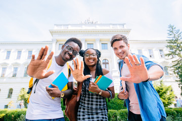 Portrait of multiethnic group of young cheerful students standing outdoors waving. Looking at...