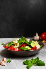 Fresh vegetable salad with mozzarella and basil. Mediterranean cuisine. Front view. Black background. Vertical. Copy space